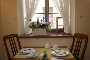A dining table set for two with floral arrangements, a window with curtains, and a view of a building outside.