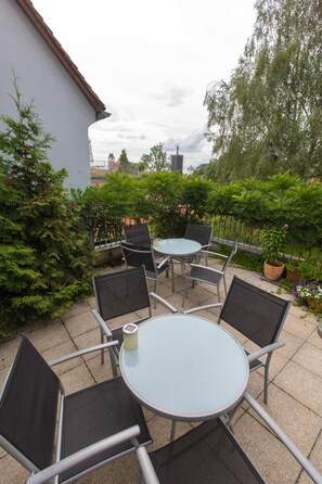 An outdoor patio with round tables and chairs, surrounded by greenery and a building. - Hotel Blaue Blume (Freiberg)