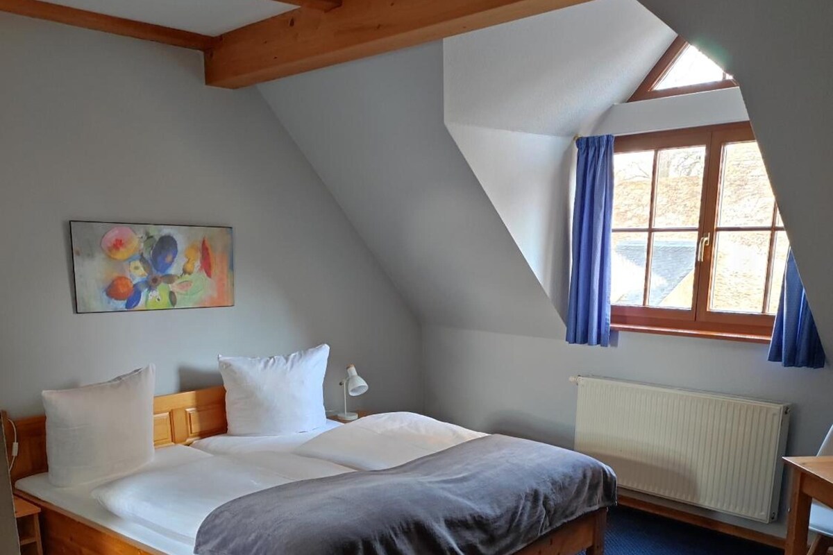 Un dormitorio con cama de madera, un radiador, una ventana con cortinas y un cuadro en la pared.