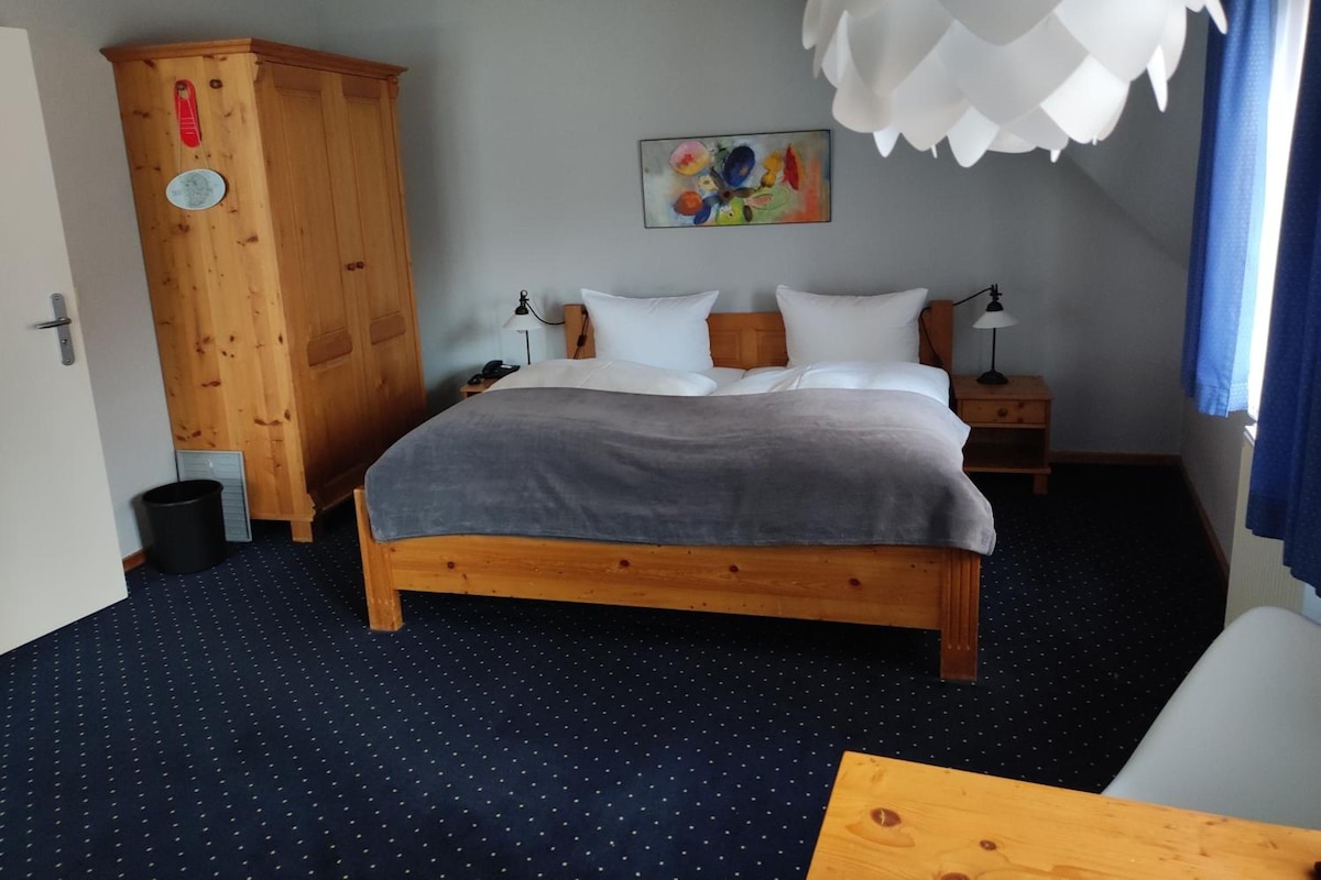 Un dormitorio con una cama de madera, una mesita de noche, un aparador, un cuadro y una lámpara en el techo.