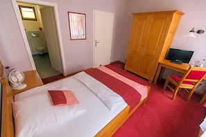 A bedroom with a bed, a wooden wardrobe, a television, and a desk.