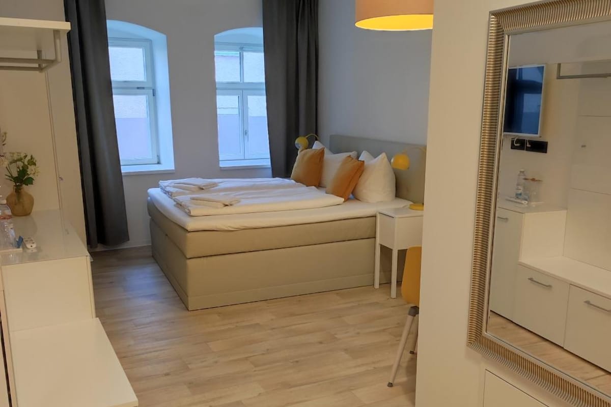 Habitación de hotel con cama, mesita de noche, espejo y ventana con cortinas.