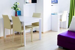 A modern room with a white desk, beige chairs, a purple bed, and a potted plant. - Hotel Blaue Blume (Freiberg)