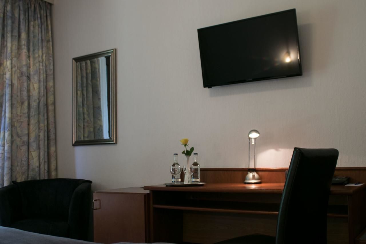 Habitación de hotel con cama, escritorio, silla, televisor montado en la pared y ventana con cortinas.