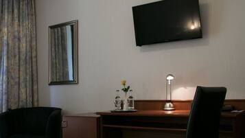 Habitación de hotel con cama, escritorio, silla, televisor montado en la pared y ventana con cortinas.