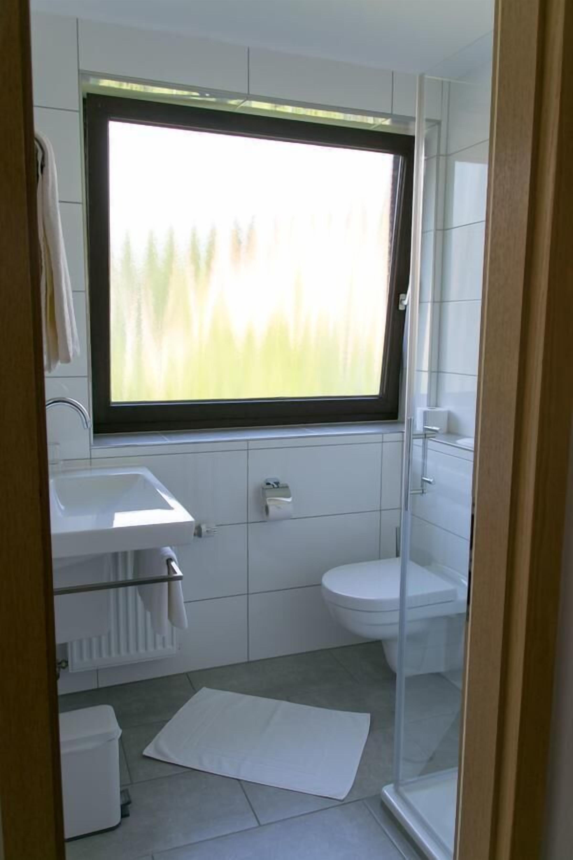 A compact bathroom with a window, a sink, a toilet, and a shower area.