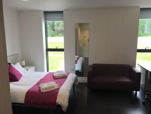 A modern hotel room with a bed, a chair, and a large window.