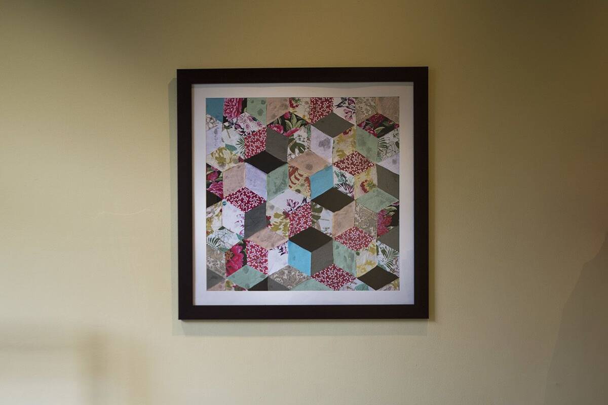 A bed with two blue pillows and a quilt hanging on the wall above it.