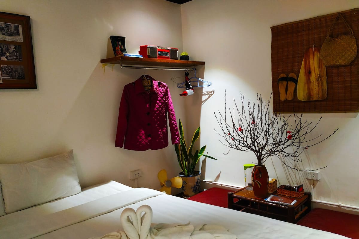 A bedroom with a bed, a hanging chair, a shelf with items, a plant, and a wall-mounted shoe rack.