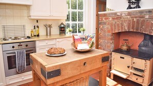 Une cuisine avec une table en bois, un four en briques et une fenêtre donnant sur un paysage verdoyant.