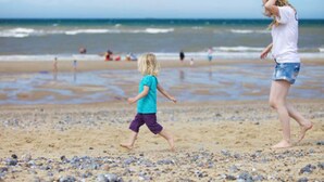 Une scène de plage où un enfant et un adulte marchent sur le sable.