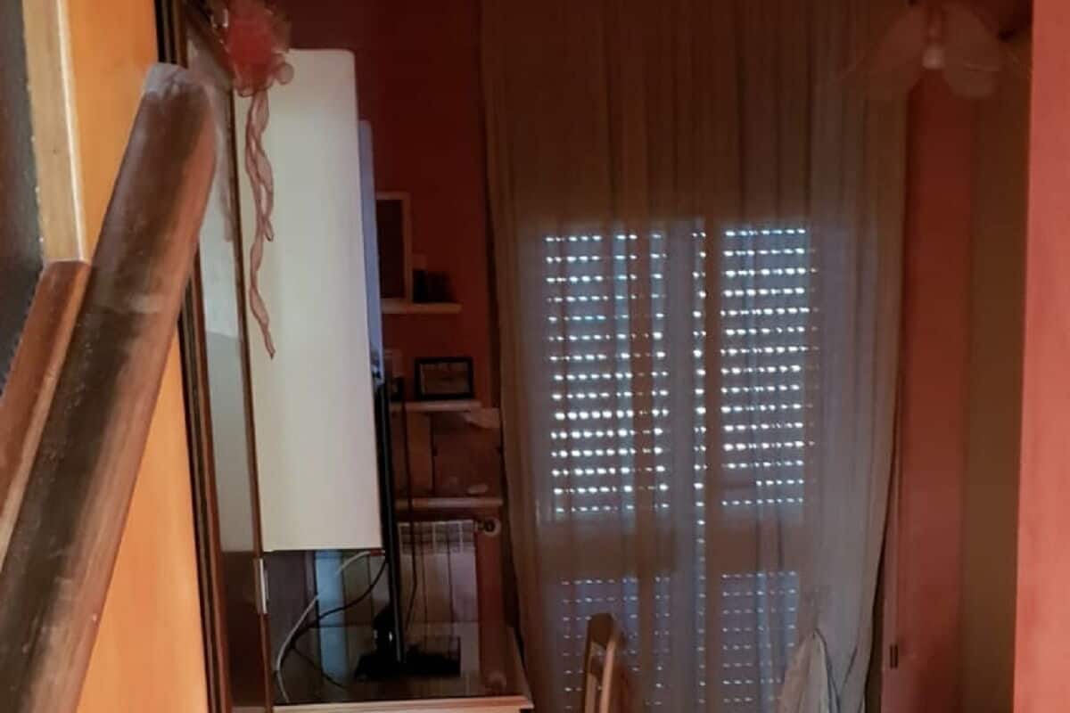 Une pièce avec un plancher en bois, un lit recouvert d’une couverture rouge, un bureau avec une chaise et une fenêtre avec des rideaux.