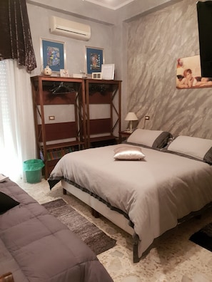 A bedroom with a bed, a wooden side table, a lamp, a green trash bin, and a framed picture on the wall. - Lussuoso B&B Palazzo Putrino (Palmi)