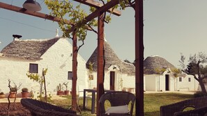 A courtyard with wicker furniture, white buildings with tiled roofs, and potted plants. - Lunalì (Alberobello)
