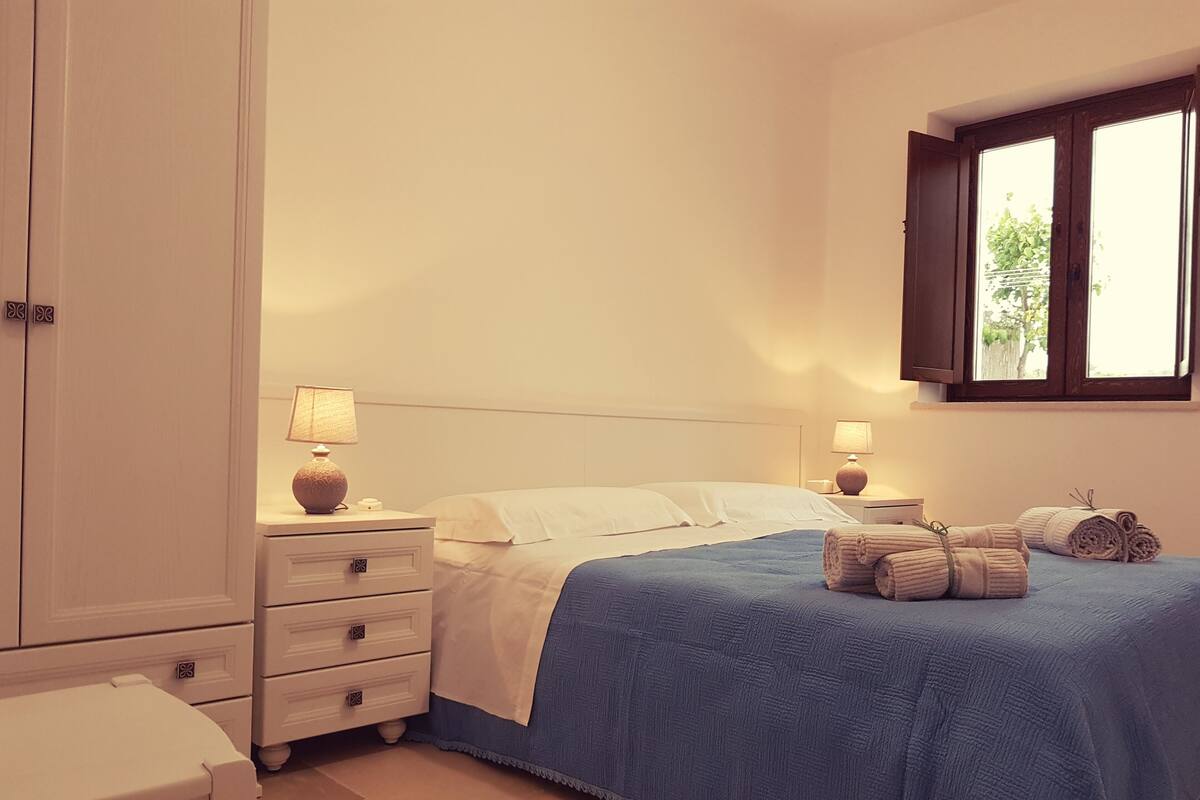 A bedroom with a bed, two bedside tables with lamps, a window, and a chair.
