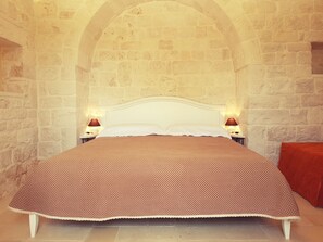 Un lit recouvert d’une couvre-lit à pois dans une pièce aux murs de pierre, avec deux lampes de chevet.