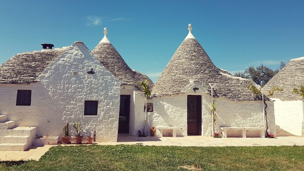 A row of traditional white buildings with conical roofs and stone walls. - Lunalì (Alberobello)