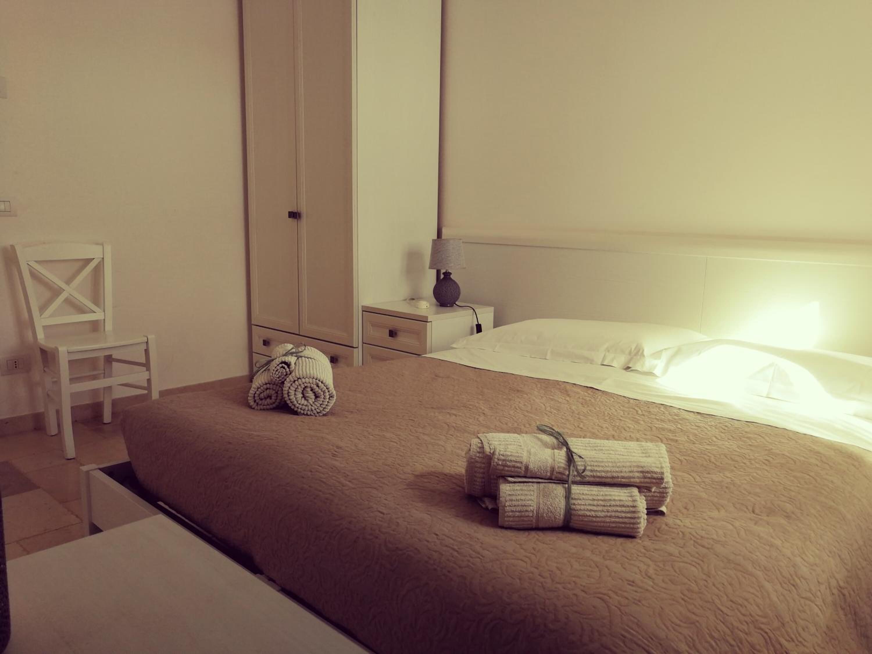 A hotel room with a bed, a chair, a wardrobe, and a nightstand with a lamp.