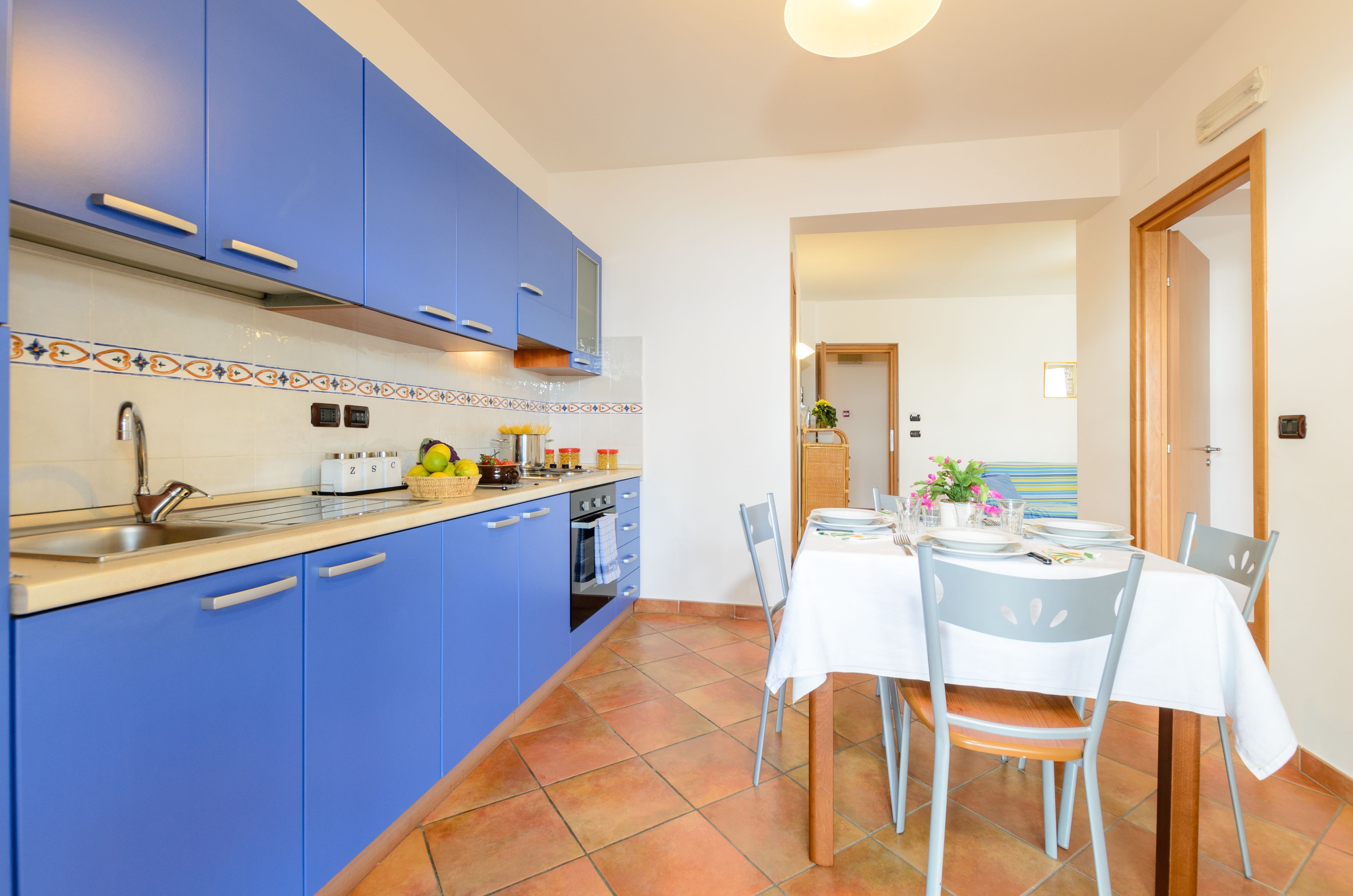 A kitchen with blue cabinets, a tiled backsplash, and a dining area with a table set for four.