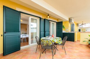 Un patio con una mesa para dos, una puerta corredera y una zona de cocina con aire acondicionado.