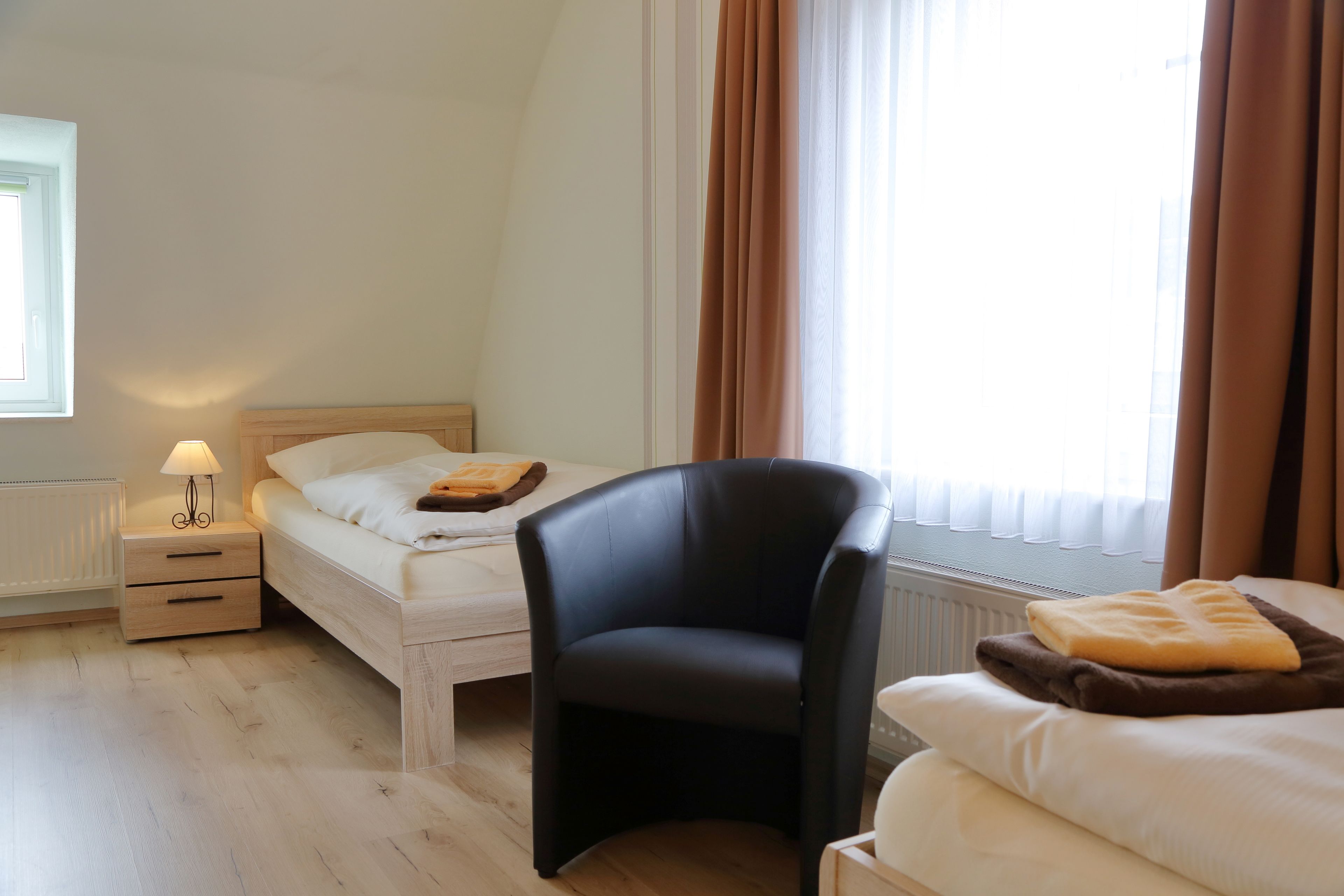 Ein Schlafzimmer mit einem Bett, einem Sessel, einem Nachttisch und einem Fenster mit Vorhängen.
