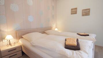 A neatly made double bed with white linens and two pillows, a bedside table with a lamp, and two wall-mounted signs with the words "Love" and "Dream".