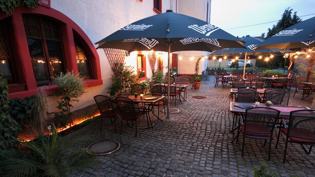 An outdoor patio with cobblestone flooring, multiple tables and chairs, and umbrellas with the logo "Le Comptoir". - Pension Gasthof und Hotel Roter Hirsch (Claussnitz)