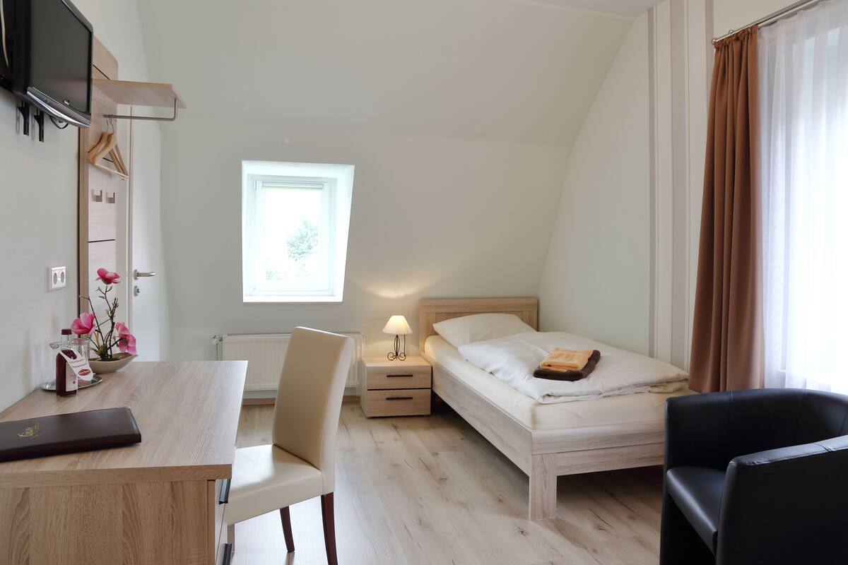 A bedroom with a bed, bedside table, lamp, and a TV mounted on the wall.