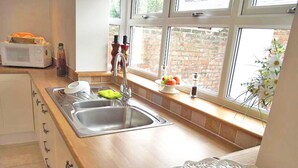 A kitchen with a sink, a microwave, and a window with a view of a brick wall. - Peel House (Gosport)