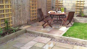 A patio with a wooden table and chairs, a red umbrella, and a stone wall with a wooden trellis. - Peel House (Gosport)