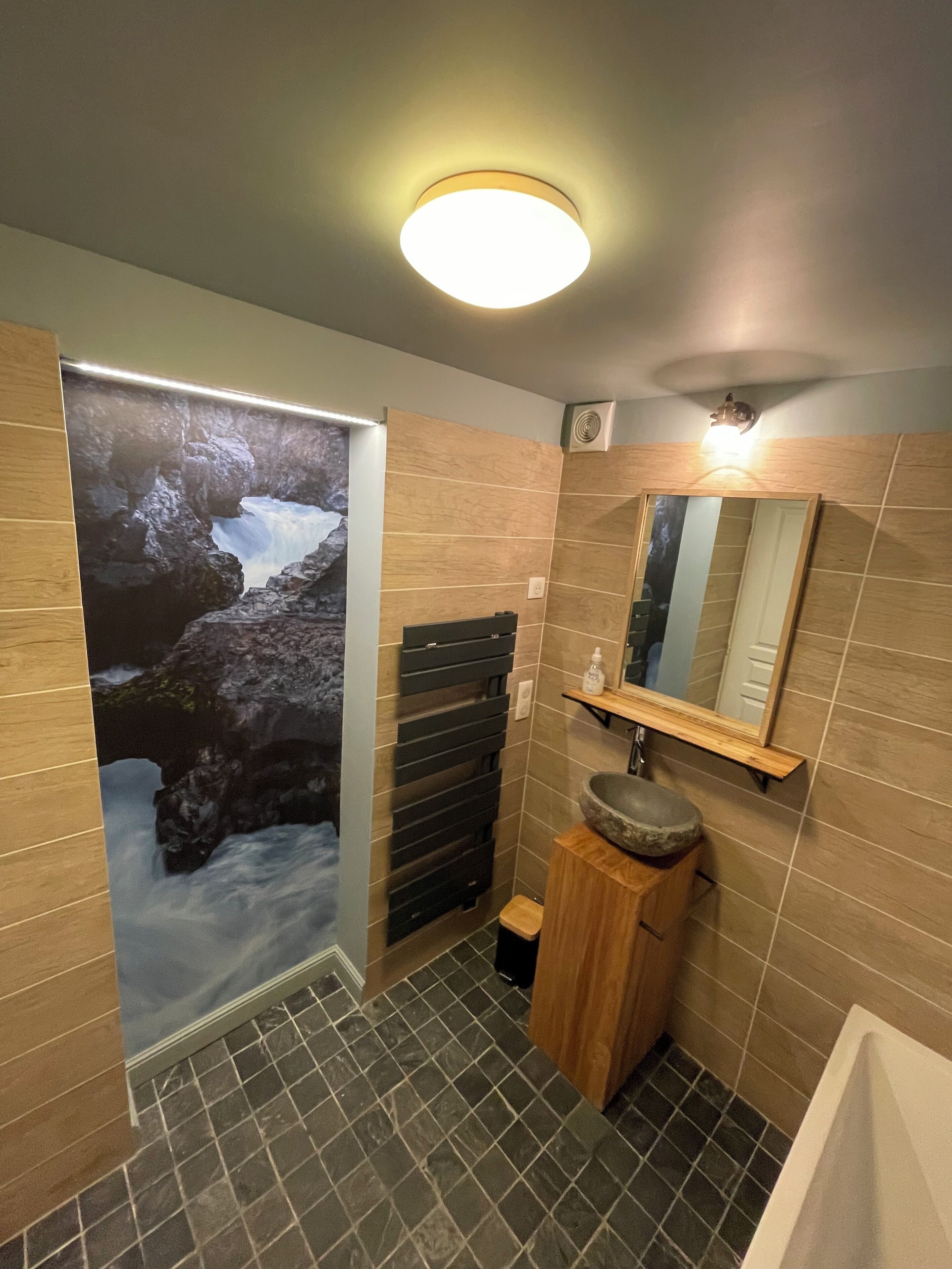 Une salle de bain avec un lavabo en pierre, un miroir au-dessus et un espace douche.
