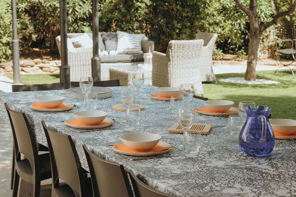 An outdoor dining area with a table set for six, surrounded by wicker chairs.