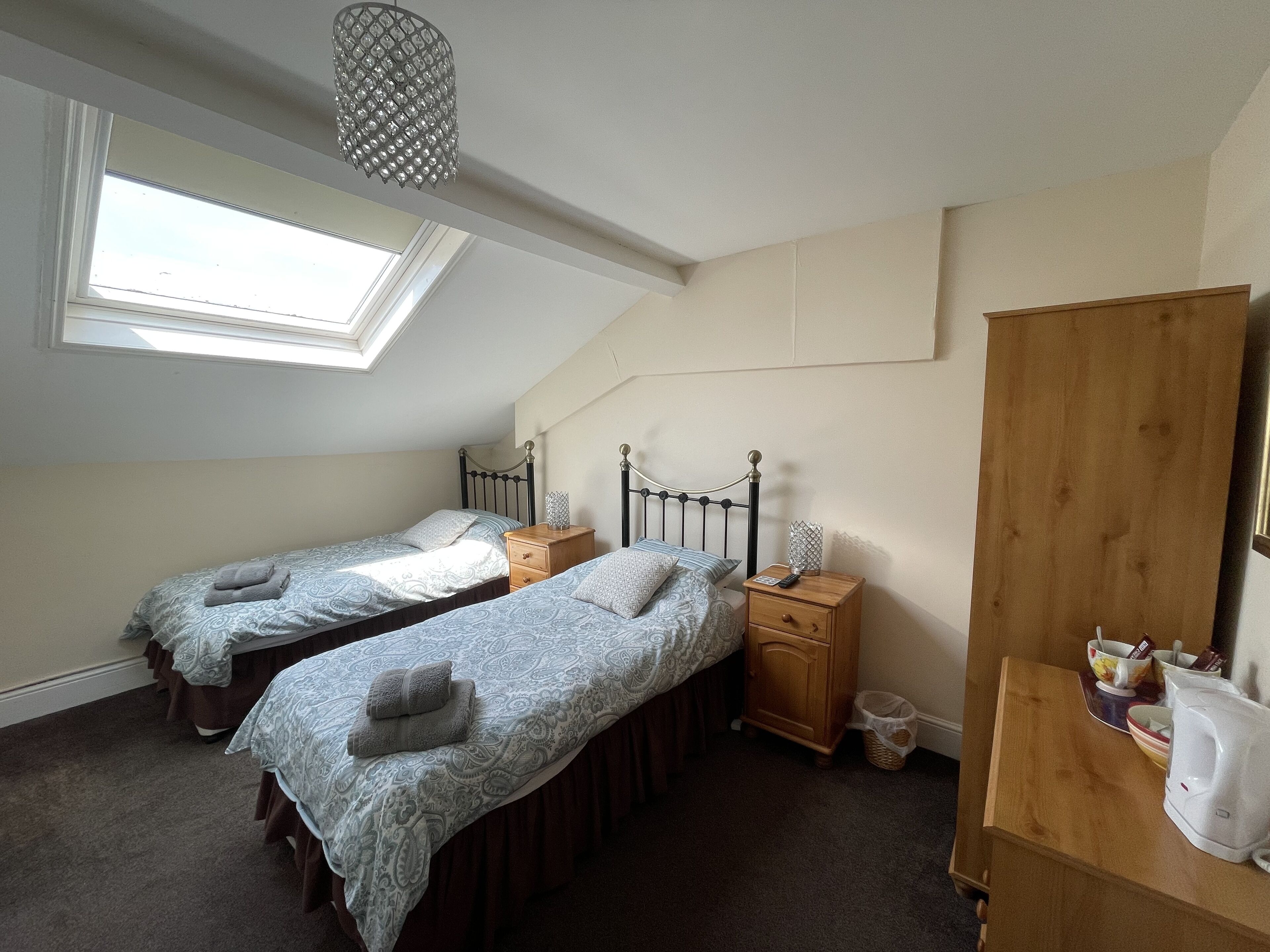 A bedroom with two single beds, a wooden nightstand, a small table, a mirror, and a skylight.