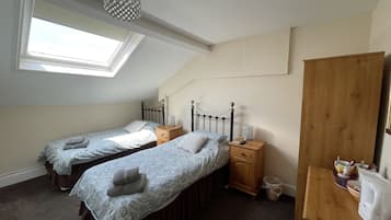 Une chambre avec deux lits simples, une table de chevet en bois, une petite table, un miroir et une fenêtre de toit.