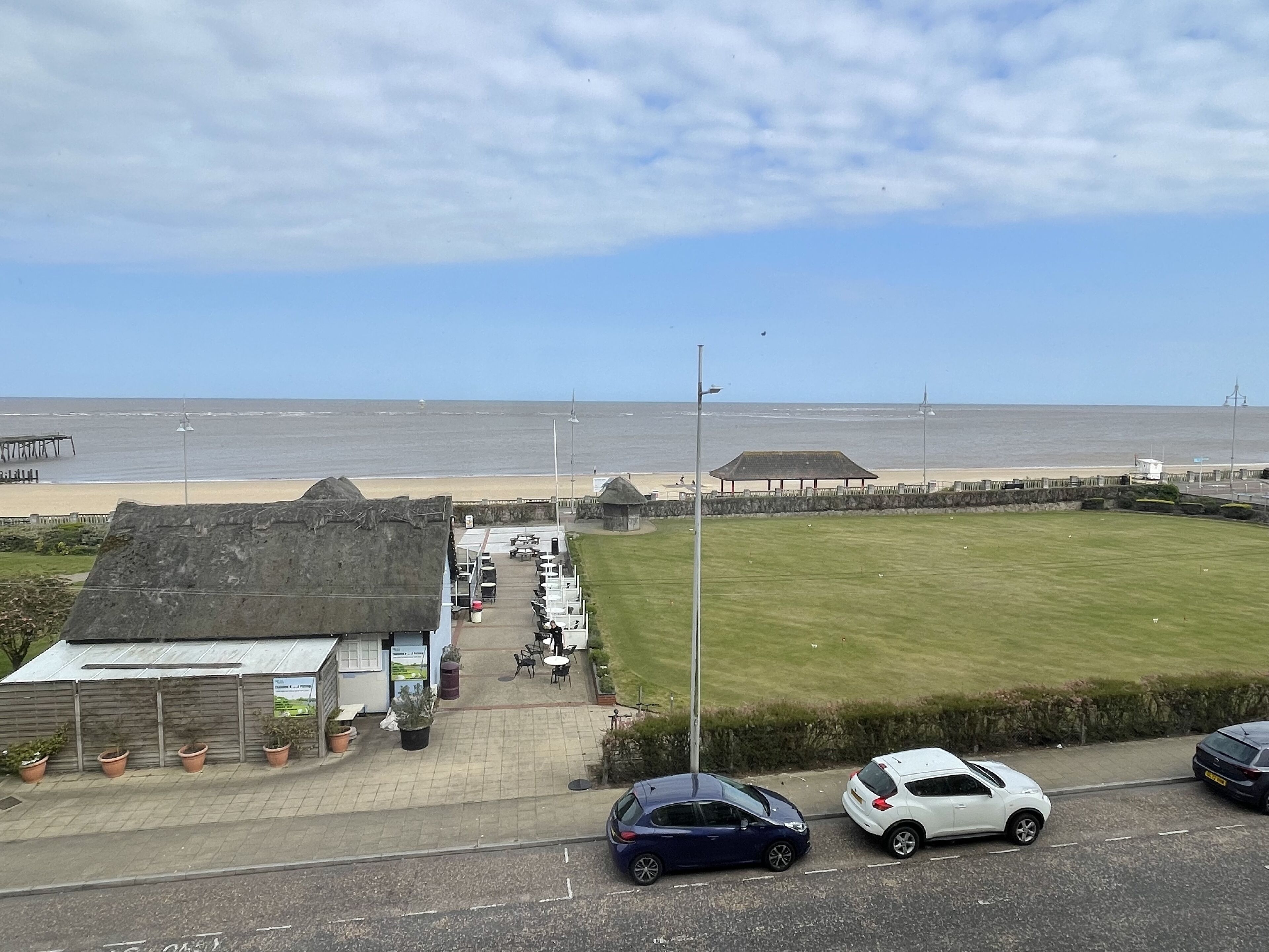 Vista costera con una zona cubierta de césped, un edificio con techo de paja y una playa al fondo.