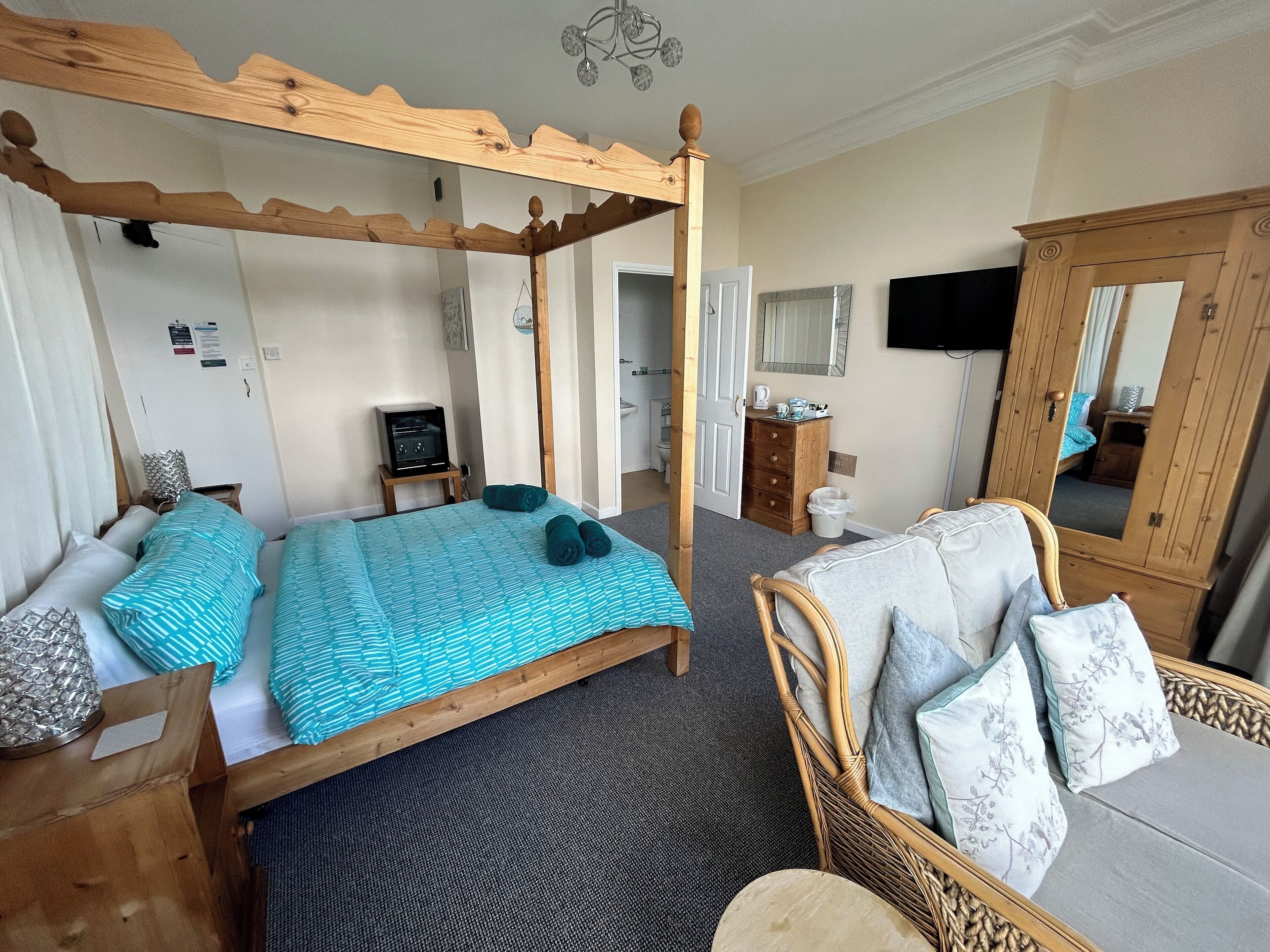 A four-poster bed with a wooden canopy, a television, a dresser, and a mirror in a hotel room.