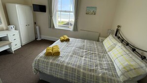 A bedroom with a bed, a desk, a wardrobe, a radiator, a window with curtains, and a painting on the wall. - Bon-ami (Lowestoft)