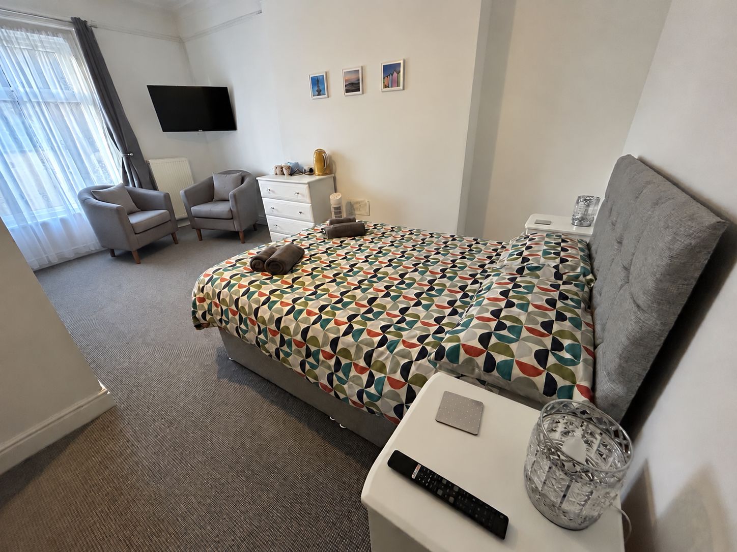 Ein Hotelzimmer mit Bett, Sessel, Schreibtisch, Fernseher und einem Fenster mit Vorhängen.