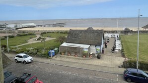 A coastal view with a pier, beach, and a small building with outdoor seating. - Bon-ami (Lowestoft)