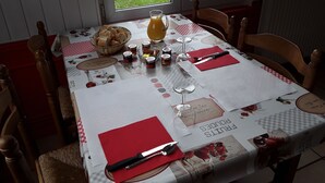 A dining table set with bread, wine glasses, and condiments, with a view of a garden through the window. - Hôtel Au Bon Coin (Colleville)