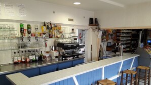 A bar area with stools, a coffee machine, and shelves with bottles and glasses. - Hôtel Au Bon Coin (Colleville)