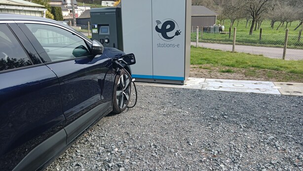 A car parked at an electric charging station with a clear view of the surrounding area including a grassy field and a building in the background. - Hôtel Au Bon Coin (Colleville)