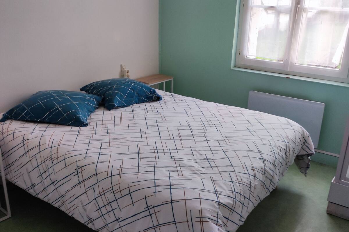 A bed with a patterned bedspread, two pillows, a nightstand, and a window with blinds.
