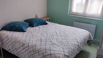Una cama con colcha estampada, dos almohadas, una mesita de noche y una ventana con persianas.