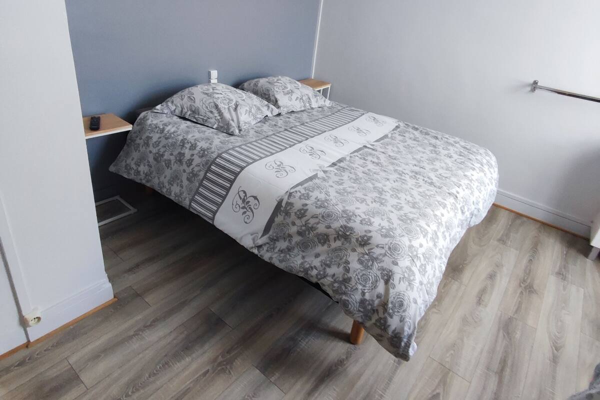 A single bed with a floral-patterned bedspread, a bedside table with a lamp, and a wooden floor.
