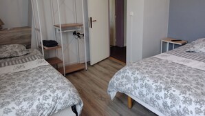 A bedroom with two beds, a wardrobe, and a door leading to another room. - Hôtel Au Bon Coin (Colleville)