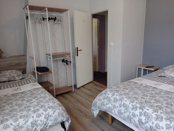 A bedroom with two beds, a wardrobe, and a door leading to another room. - Hôtel Au Bon Coin (Colleville)