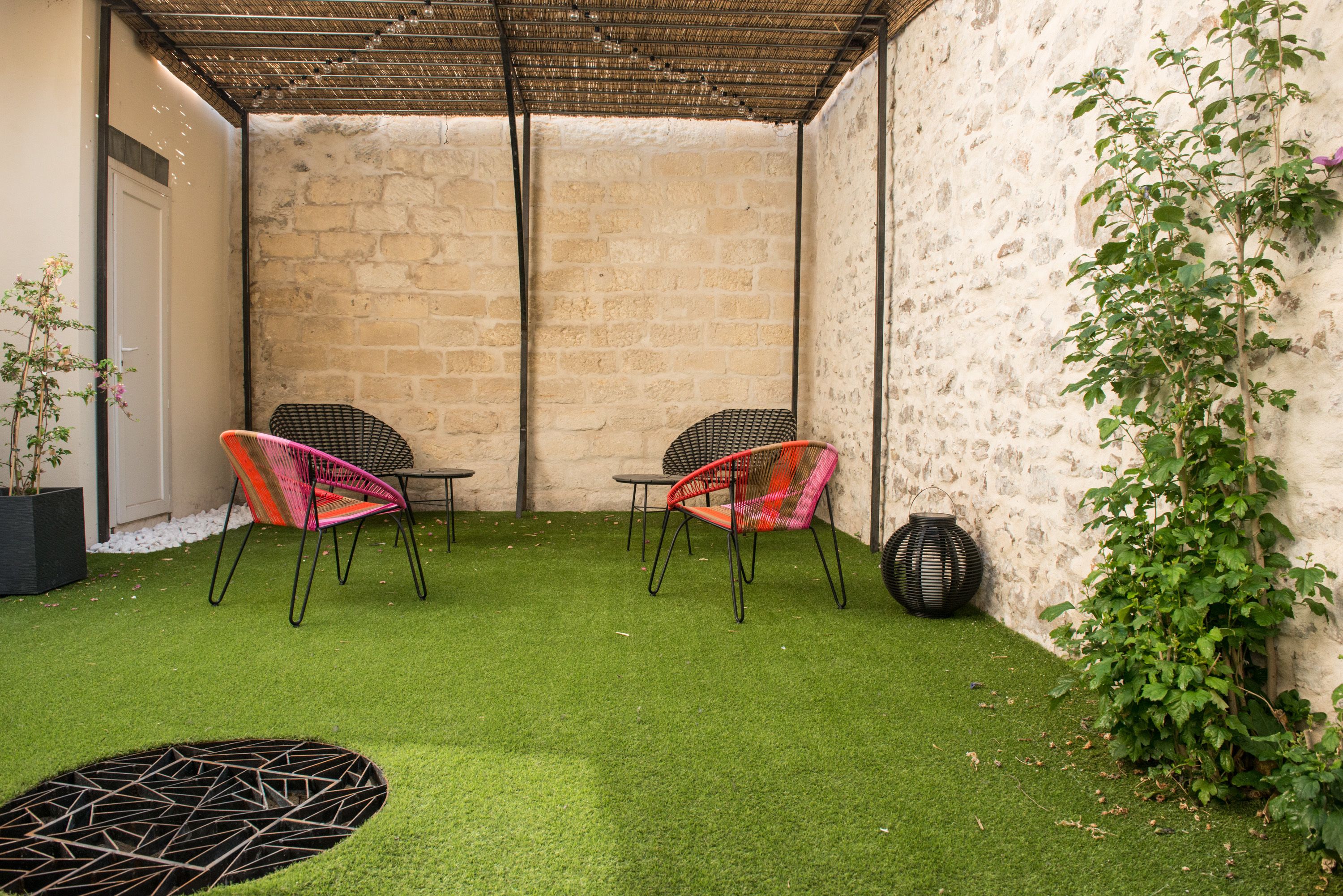 Une cour avec une pelouse artificielle, deux fauteuils en osier, une petite table et une plante en pot.