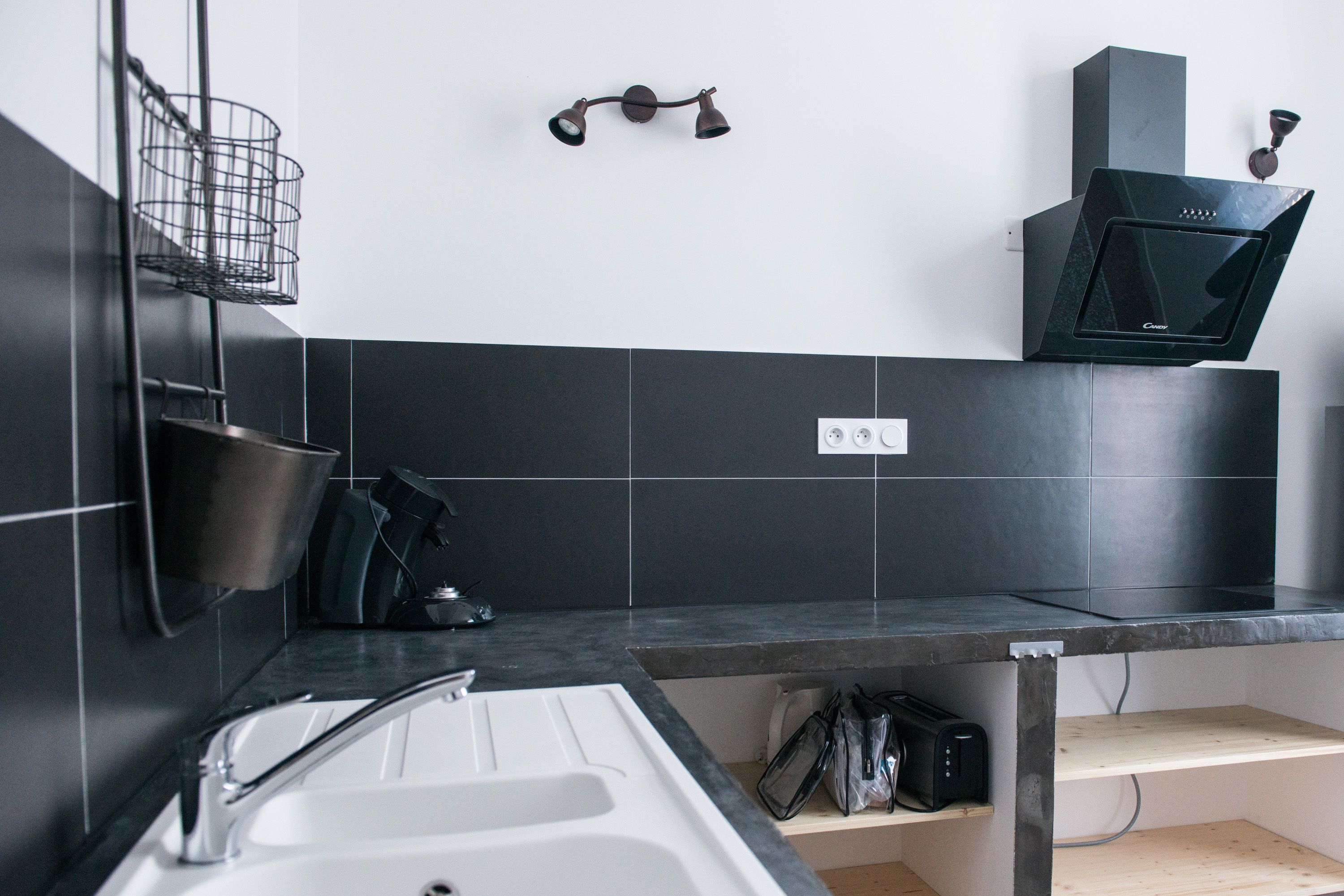 Una cocina moderna con un lavamanos blanco, baldosas negras, un microondas negro y una campana extractora negra.