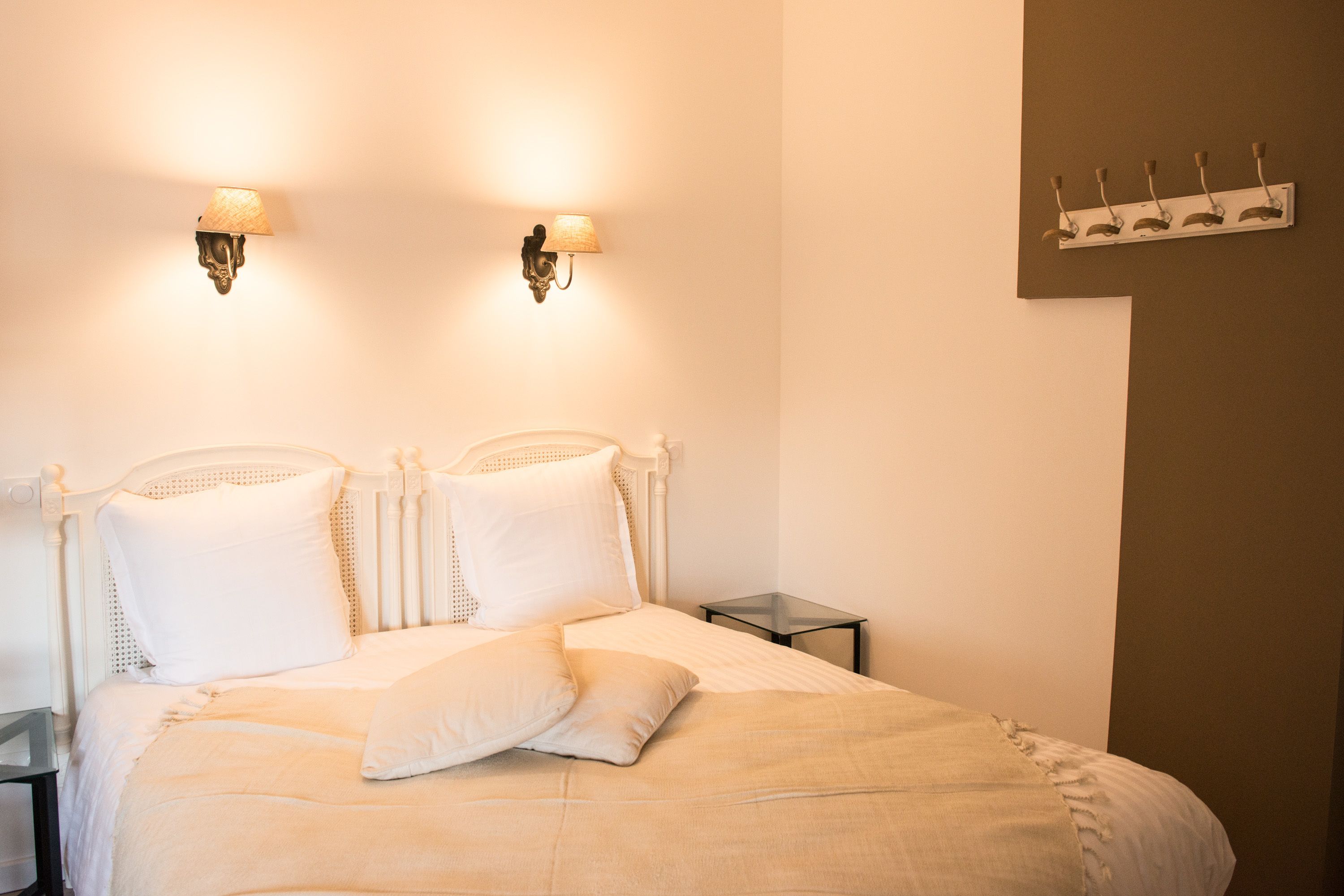 Un letto rifatto con lenzuola bianche, due lampade a parete e un comodino.